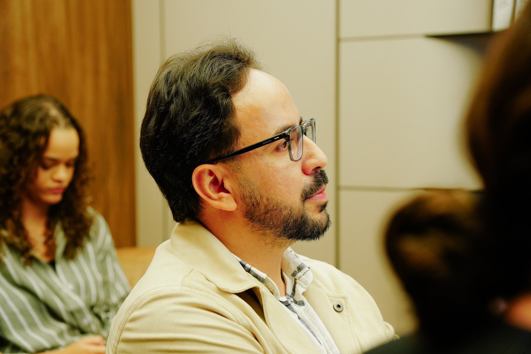 Participante de perfil, de óculos e jaqueta bege, ouvindo atentamente durante o workshop.
