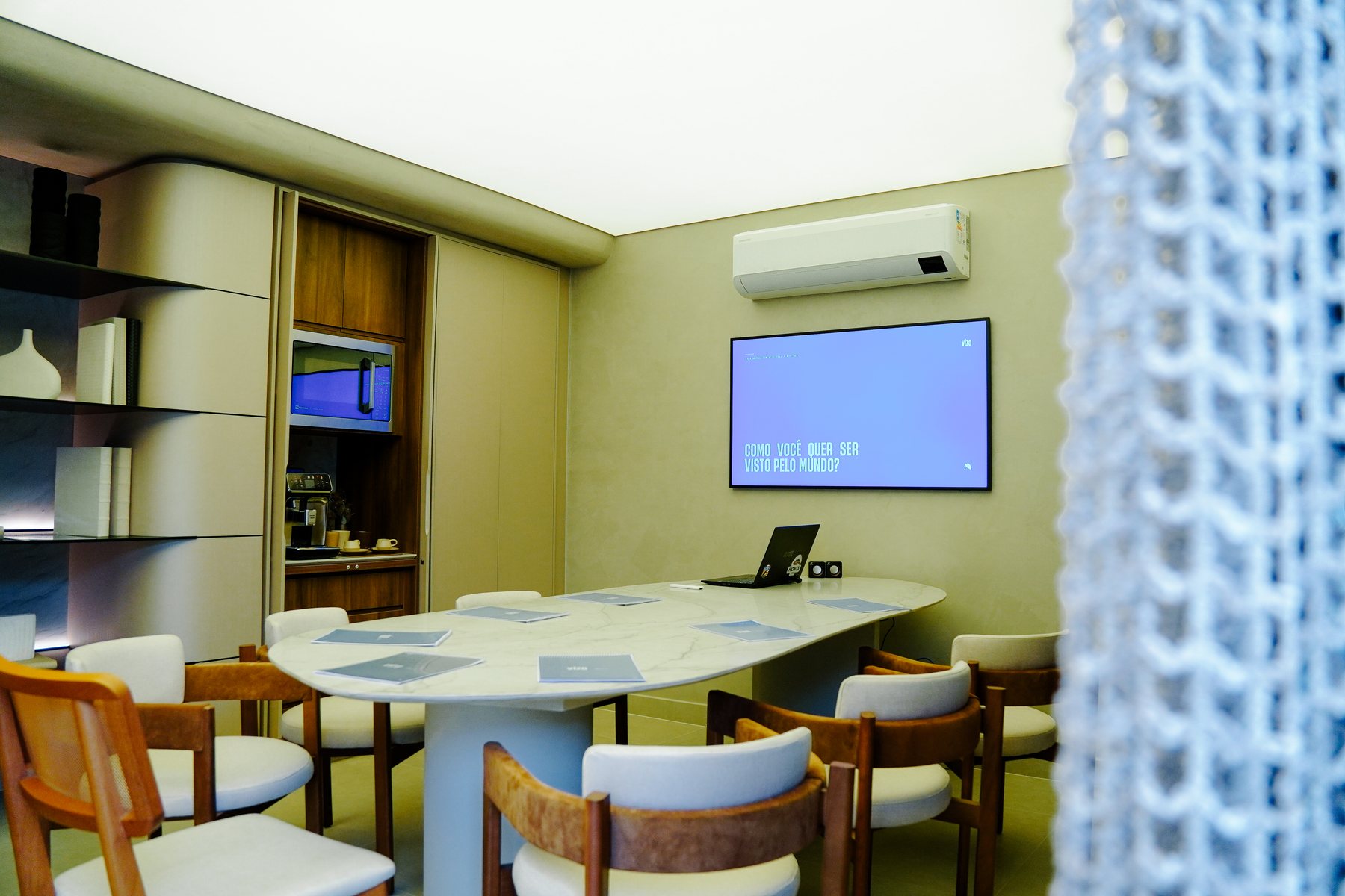 Sala de reunião preparada para o workshop, com cadernos sobre a mesa e a pergunta “Como você quer ser visto pelo mundo?” na TV.