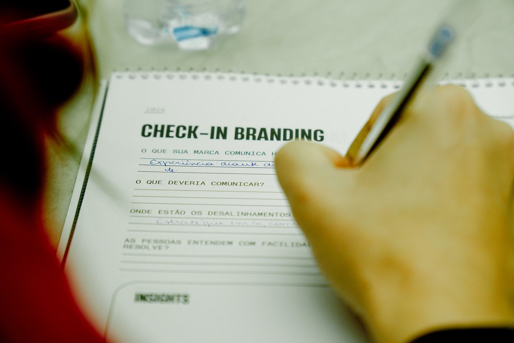 Detalhe de uma mão escrevendo no caderno “Check-in Branding” do workshop.